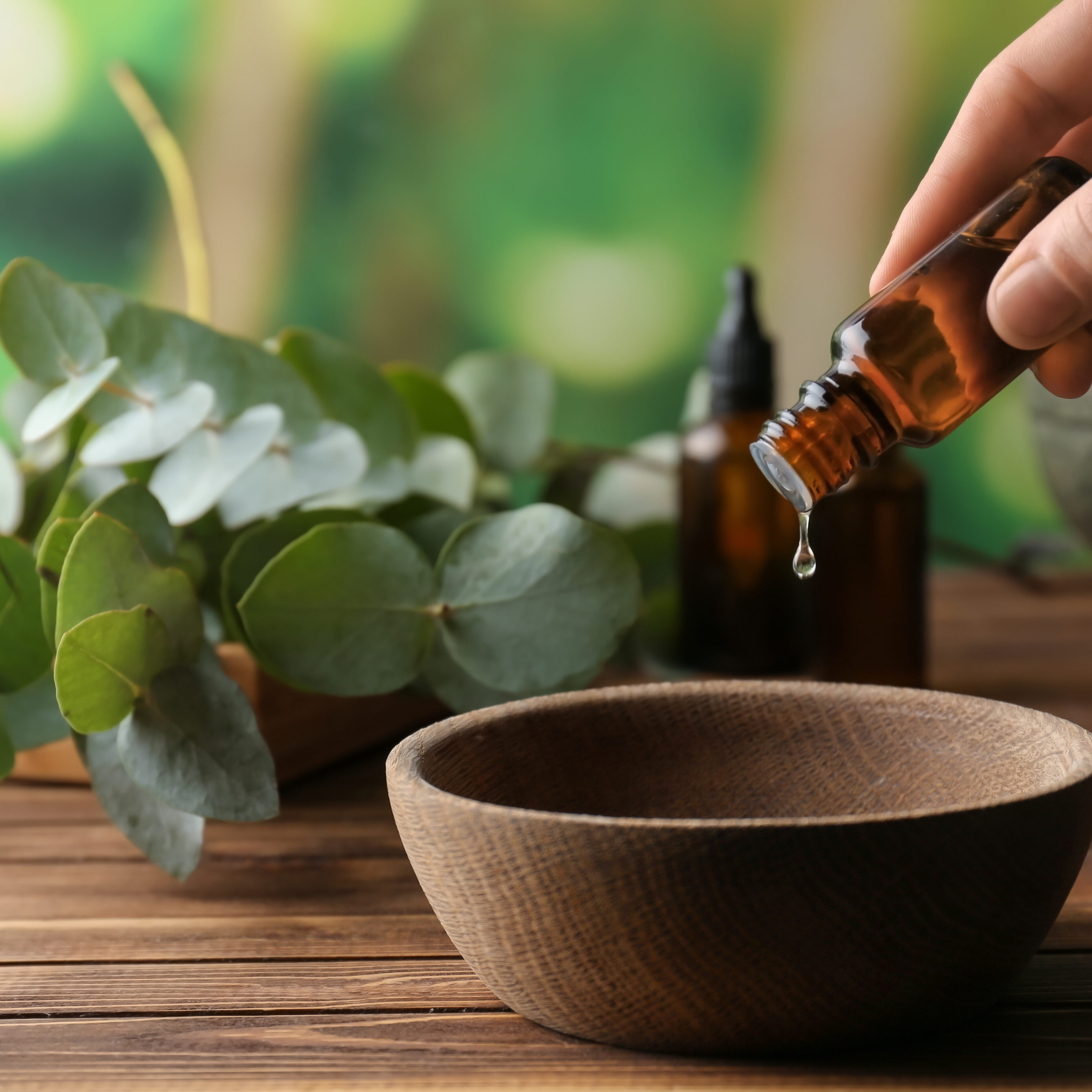 Woman pouring eucalyptus essential oil into bowl on wooden table