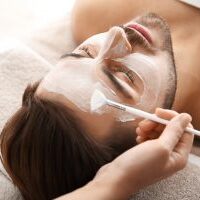 Cosmetologist applying mask on client's face in spa salon