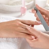 Manicurist filing client's nails at table, closeup. Spa treatment