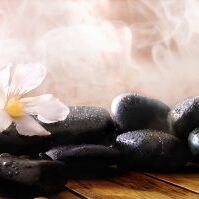 Group of black stones on wood base, steam background. Sauna, therapy, relaxation, and health concept.